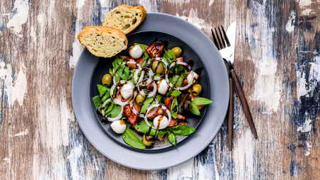 Mediterranean salad with fresh green salad with mozzarella, tomatoes, olives, onion and balsamic dressing. Italian traditional cuisine. Top view. Food bannerの写真素材