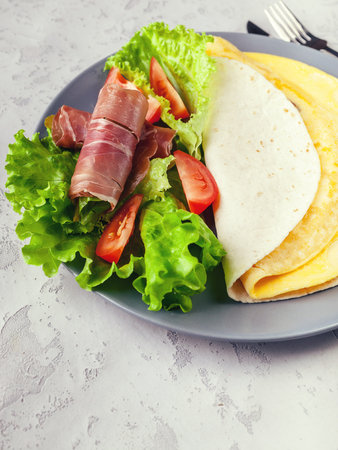Close-up omelet in wheat tortilla, lettuce, tomatoes and smoked beef. Tasty breakfastの写真素材