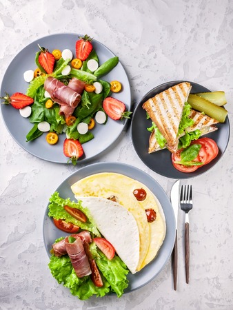 Omelet in wheat tortilla, salad with strawberries and sandwiches. Delicious and healthy breakfast. Top viewの写真素材