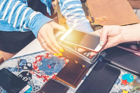 The woman pays for a purchase with a smartphone. Graceful female hands in the frame.