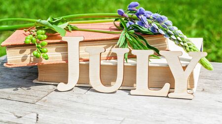 Word July, stack of old books and bouquet of flowers on a white wooden rustic background. Summer compositionの写真素材