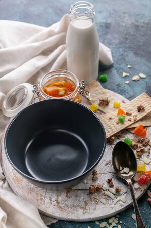 Empty dark bowl, candied fruit, orange jam and milk. Tasty and healthy breakfast concept. Vertical shotの写真素材