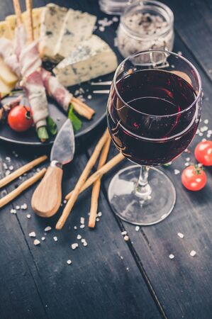 Close-up glass of red wine, snacks, jamon, cheese, cherry tomatoes and arugula. Vertical shotの写真素材