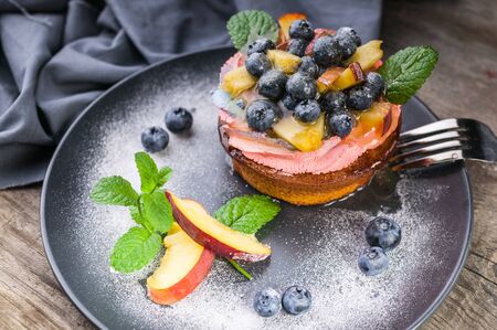 Close up of juicy peach and blueberry dessert with cream on a dark plateの写真素材