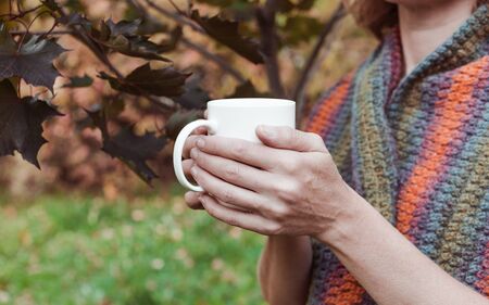 Elegant female hands hold a white cup with a hot drink. Autumn background. Close-Up