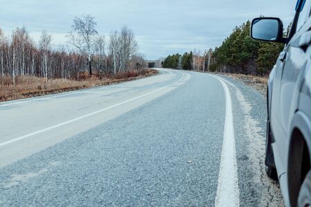 Black car on an abandoned road against the backdrop of an autumn forest. Mystical and terrible atmosphereの写真素材