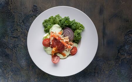 Salad with crab meat, avocado, fresh vegetables and red salmon caviar on a white plate. Top view. Horizontal shotの写真素材