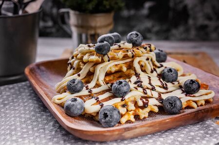 Close-up waffles with butter cream, chocolate and blueberries. Sweet dessert. Homemade baking.の写真素材
