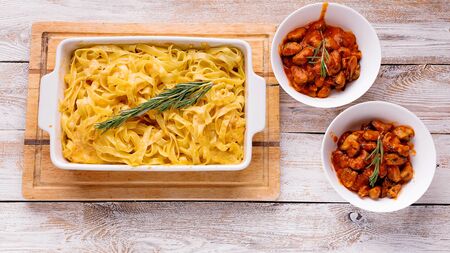 Food banner. Baked fettuccine with cheese and smoked sausage in a ceramic bowl and mussels in tomato sauce on a wooden table. Italian pastaの写真素材