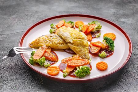 Close-up fillet of sea bass with vegetables. Baked fish, cauliflower and carrots on a plate on a gray background.の写真素材