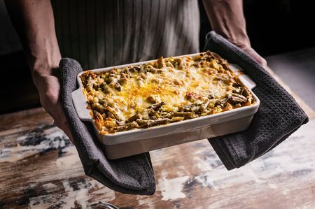 Female hands hold ceramic dishes with vegetable lasagna with green beans and cheese. Healthy...