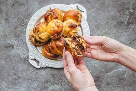 Top view. Female hands hold sweet homemade chocolate-nut buns on a silver platter.