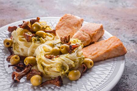 Close-up of fried salmon, tagliatelle with pesto sauce, fried chanterelles and olives. Seafood and Italian Pastaの写真素材