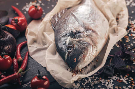 Fresh raw dorado. Fish, spices, chili peppers, salt, onions, tomatoes and basil on a dark wooden table. Close up. Sea foodの写真素材