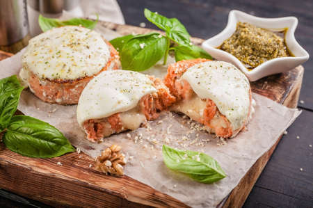 Salmon cutlets with cheese, walnuts, pesto and basil on a wooden cutting board. Delicious and healthy seafood dishes. Cooking like in a restaurantの写真素材