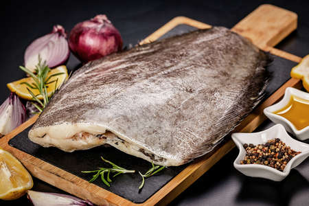 Halibut raw fillet on a wooden cutting board on a dark background. Red onion, salt, pepper and spicesの写真素材