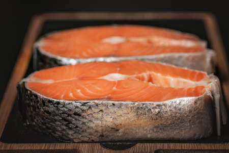 Close-up raw wild salmon steak on a cutting board on a dark background. Source of Beneficial Omega-3...