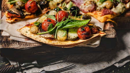Close-up delicious pizza with vegetables, mozzarella, olives and herbs on a cutting board on a dark background. Mediterranean Kitchen. Top viewの写真素材