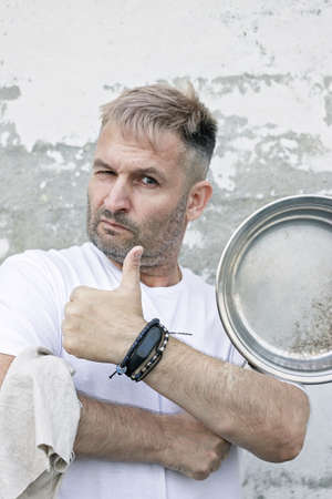 Chef in a white T-shirt with a frying pan in his hands. He has extended arm with thumbs up. Caucasian man on a brick wall background. Vertical shotの写真素材