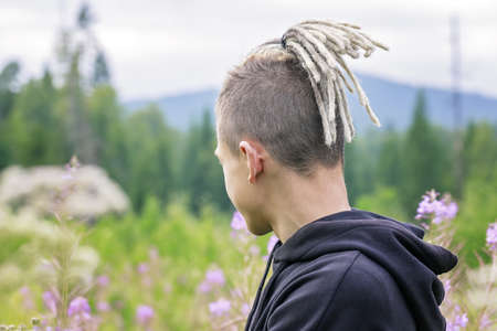 Portrait of a young guy with dreadlocks against the backdrop of a forest park and mountains. View from the back. Copy spaceの写真素材