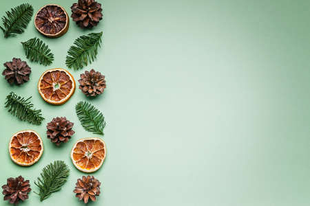 Christmas border of green fir branches, cones and dried oranges on a light green background....