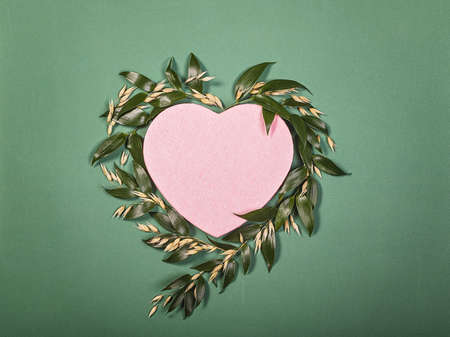 Frame made of natural flowers, leaves and grains of oats in the shape of a heart on a green background. Blank postcard or congratulations for Valentine's Day. Top viewの写真素材