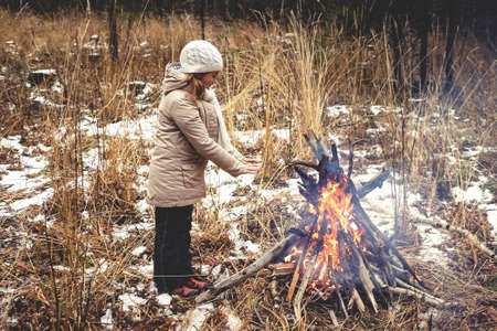 Teen girl warms his hands by the fire. Hiking in the forest concept. Late autumnの写真素材