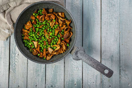 Fried chanterelles with vegetables in a pan. Edible mushrooms and green peas. Vegeterian food. Top view. Copy spaceの写真素材