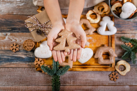 Girl hands hold gingerbread in the shape of a Christmas tree. Wooden planks Christmas background. Top viewの写真素材