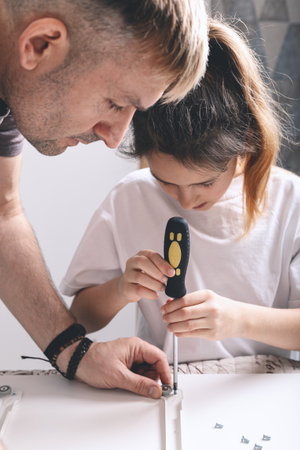 Father and daughter are assembling white furniture. Vertical shot. Selective focusの写真素材