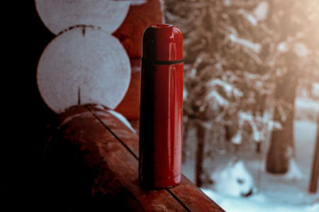 Red flask with a hot drink. Winter forest background. Low key lightingの写真素材