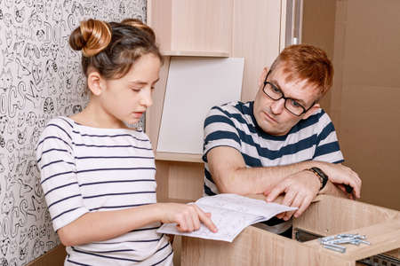 Little beautiful girl helps her concentrated father to assemble furniture at home. Caucasian family. Spending time together. Moving in.の写真素材
