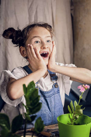 cute surprised girl with hairbuns is having fun during planting of flowers. home gardening. caucasian ethnicity. front view. vertical shot.の写真素材