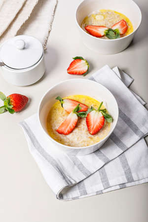 Classic oatmeal with butter and fresh fruit. Sweet strawberries. Delicious and healthy breakfast. Food still life on a light background. Ideas and recipes for home meals. Vertical shotの写真素材