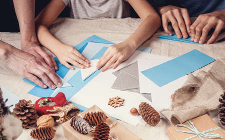 Hands of a caucasian mother and her daughter are cutting paper snowflakes with scissors. Handmade, christmas decorations, family winter activity. Close-up. Banner formatの写真素材