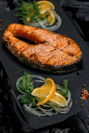 Vertical shot appetizing grilled salmon steak on a black ceramic board. Sea fish. Natural food.