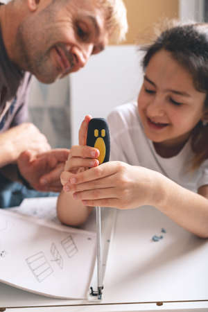 LIttle smiling cute caucasian girl and her beautiful father are assembling furniture with a screewdriver following the instruction. Housework. Front view.の写真素材