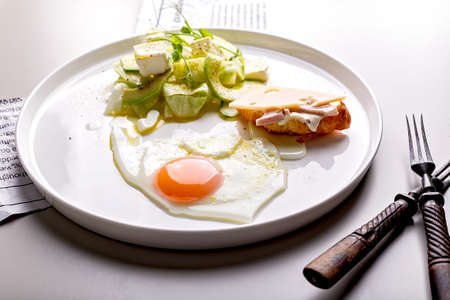 Delicious and healthy breakfast. Fried egg and vegetable salad with avocado and herbs. Mini croissant with ham and cheese on a round white plate. Organic foodの写真素材
