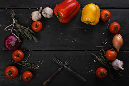 Red and yellow bell peppers, fresh tomatoes, onions and forks on a black wooden background. Vegetables on a table, dark colored flatlay, top view.の写真素材