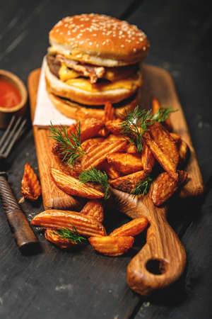 Appetizing double beef burger and a serving of fries on a wooden cutting board. Rustic dark...