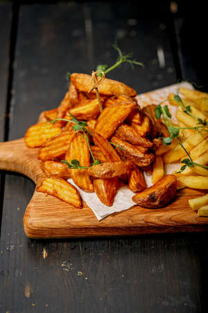 Close-up fried potato wedges on a wooden cutting board. Big portion of baked potatoes with sauce and...