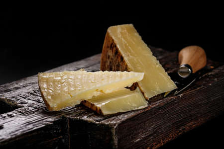 Close-up of Cheddar cheese. Semi-soft aged cow's milk cheese according to an old English recipe. Piece of cheese on a dark wooden board and knife for cutting cheese. Low key image. Copy spaceの写真素材