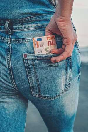 A woman's hand takes out euro bills from the back pocket of her jeans. The concept of finance,...
