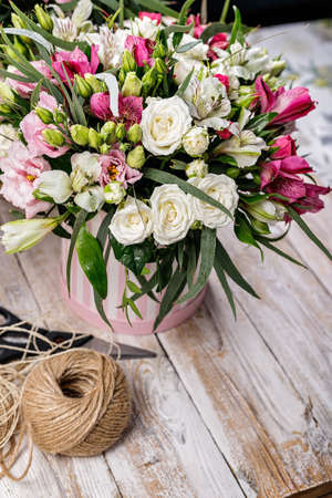 Gift bouquets of flowers to a cardboard box, packing twine and scissors. Pink rose and alstrameria...