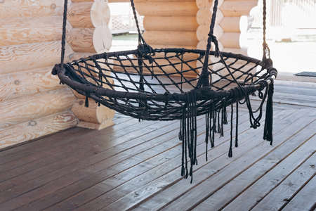 Hanging round hammock chair for relaxing on the open terrace of a wooden house. Country rest and...