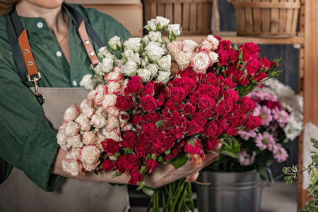 Woman florist is holding a large bouquet of roses. Florist workplace. Small business concept. Flowers and accessories shop. Close-upの写真素材