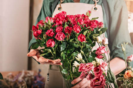 Woman florist is holding a large bouquet of roses. Florist workplace. Small business concept. Flowers and accessories shop. Close-upの写真素材