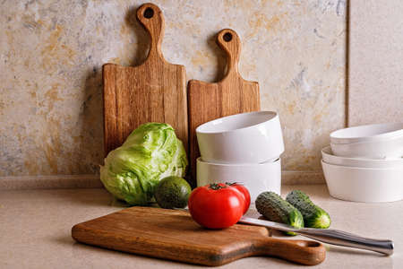 Delicious and healthy vegetables. Kitchen accessories. Chopping wooden boards and utensils. Ripe tomatoes, fresh cucumbers and crispy ice salad, avocado. Natural organic food. Modern kitchen stilllifeの写真素材