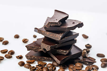 A stack of dark cracked chocolate and black coffee beans on a white background. Pieces of bitter chocolate. Food photography. Close-up.の写真素材