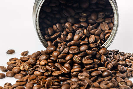 Open tin can and grains of black coffee on a white background. Fragrant roasted arabica beans on a white table. Traditional morning drink. Copy space. Coffee time themeの写真素材